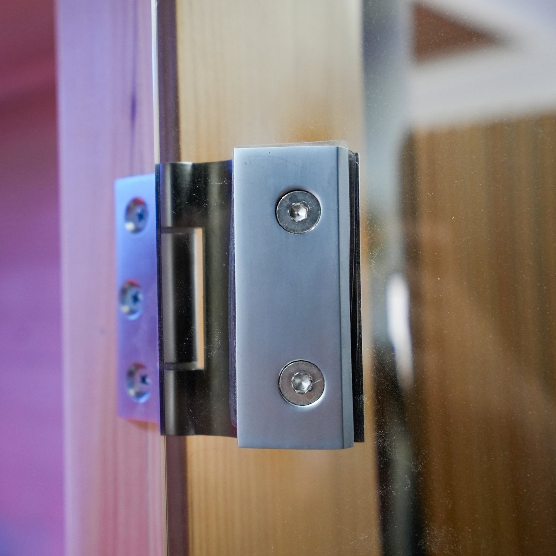 Close-up of a metal hinge on a glass and wood sauna door
