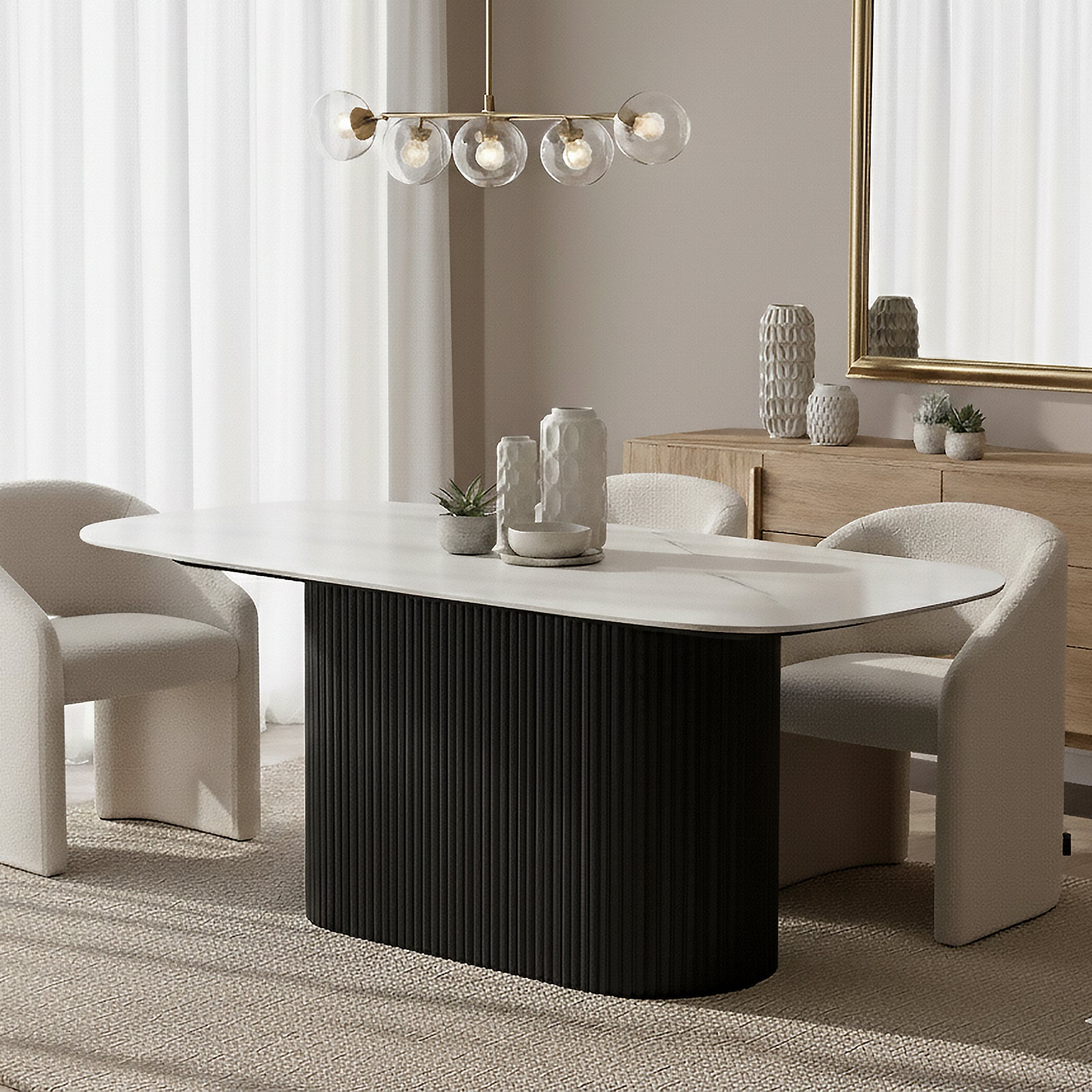 Aeris 180cm Marble Look Dining Table With Wood Base in Black, featuring an elegant white oval tabletop on a fluted black pedestal, surrounded by off-white boucle chairs and accented with sculptural vases.