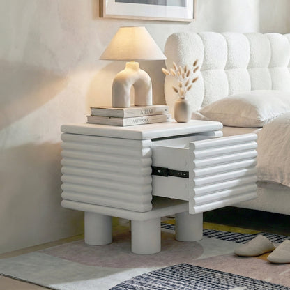 White ribbed nightstand in a modern bedroom next to a bed with lamp and books