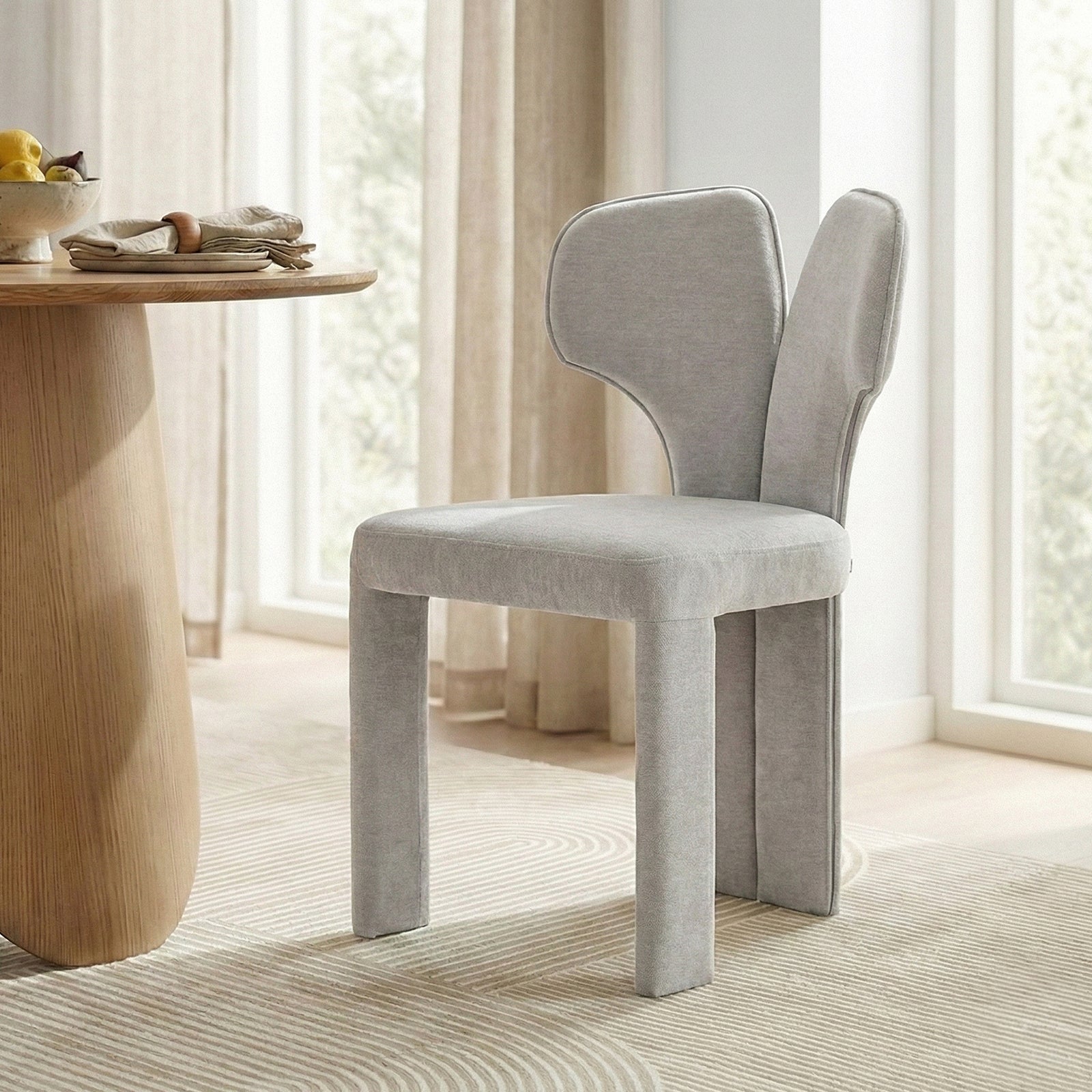 Two light gray upholstered chairs by a wooden dining table in bright room