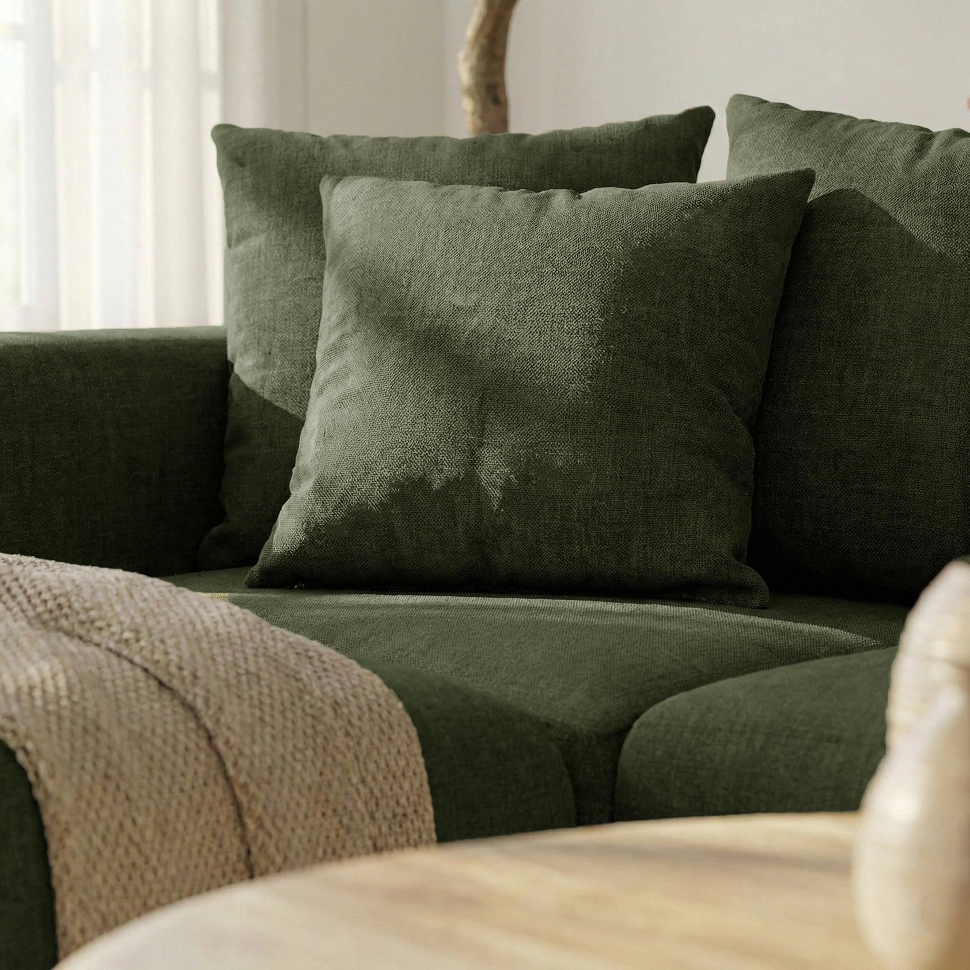 Close-up corner of dark green sectional sofa with pillows and throw in a bright room