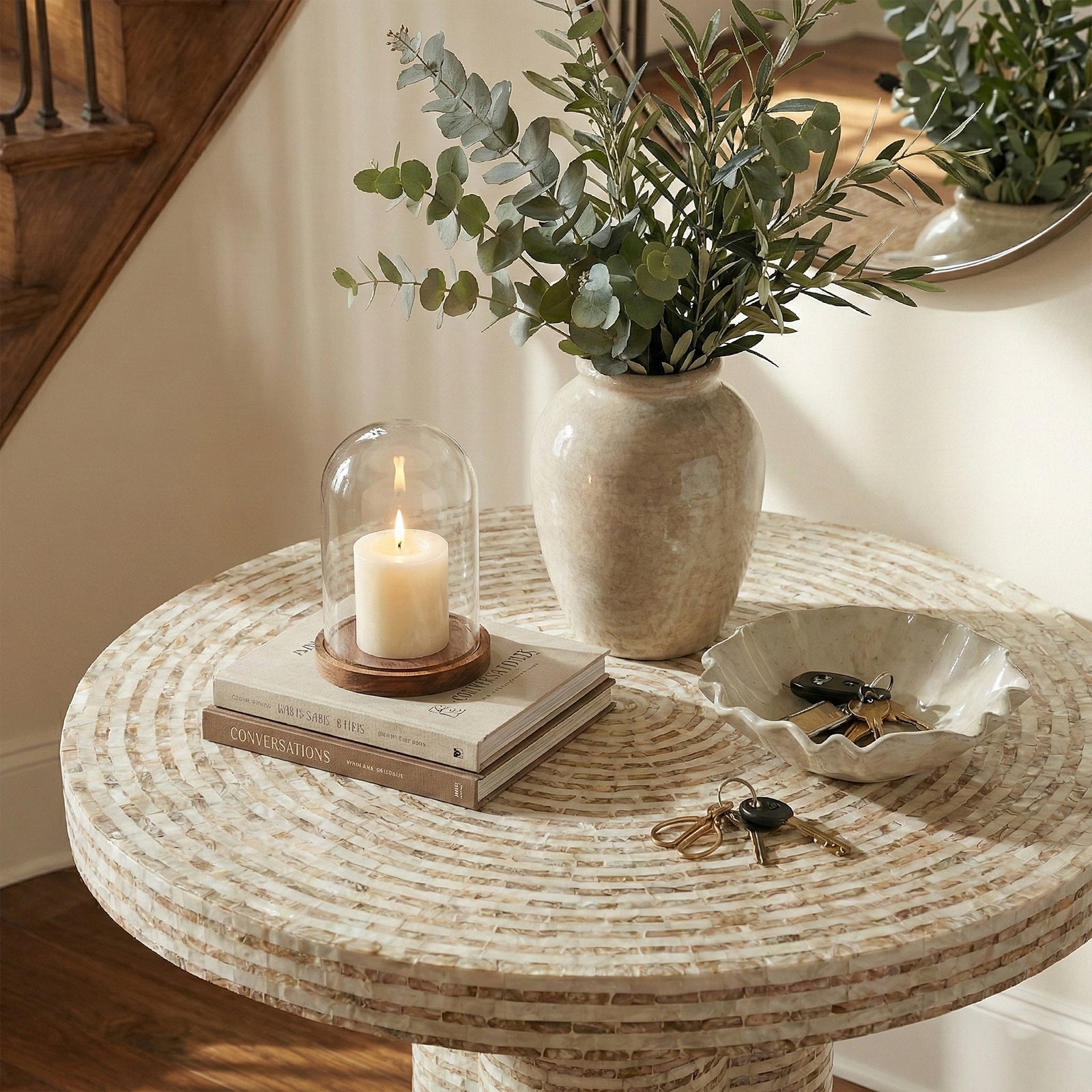 Partial view of mosaic table surface styled with vase, candle under cloche, and dish