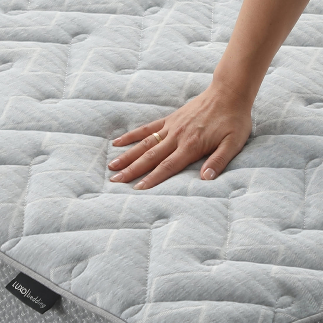 Hand pressing on quilted mattress surface with brand tag visible