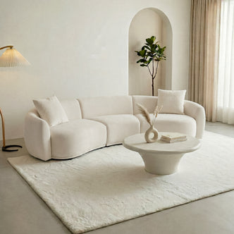 Cream curved sectional sofa in a modern living room with coffee table and rug
