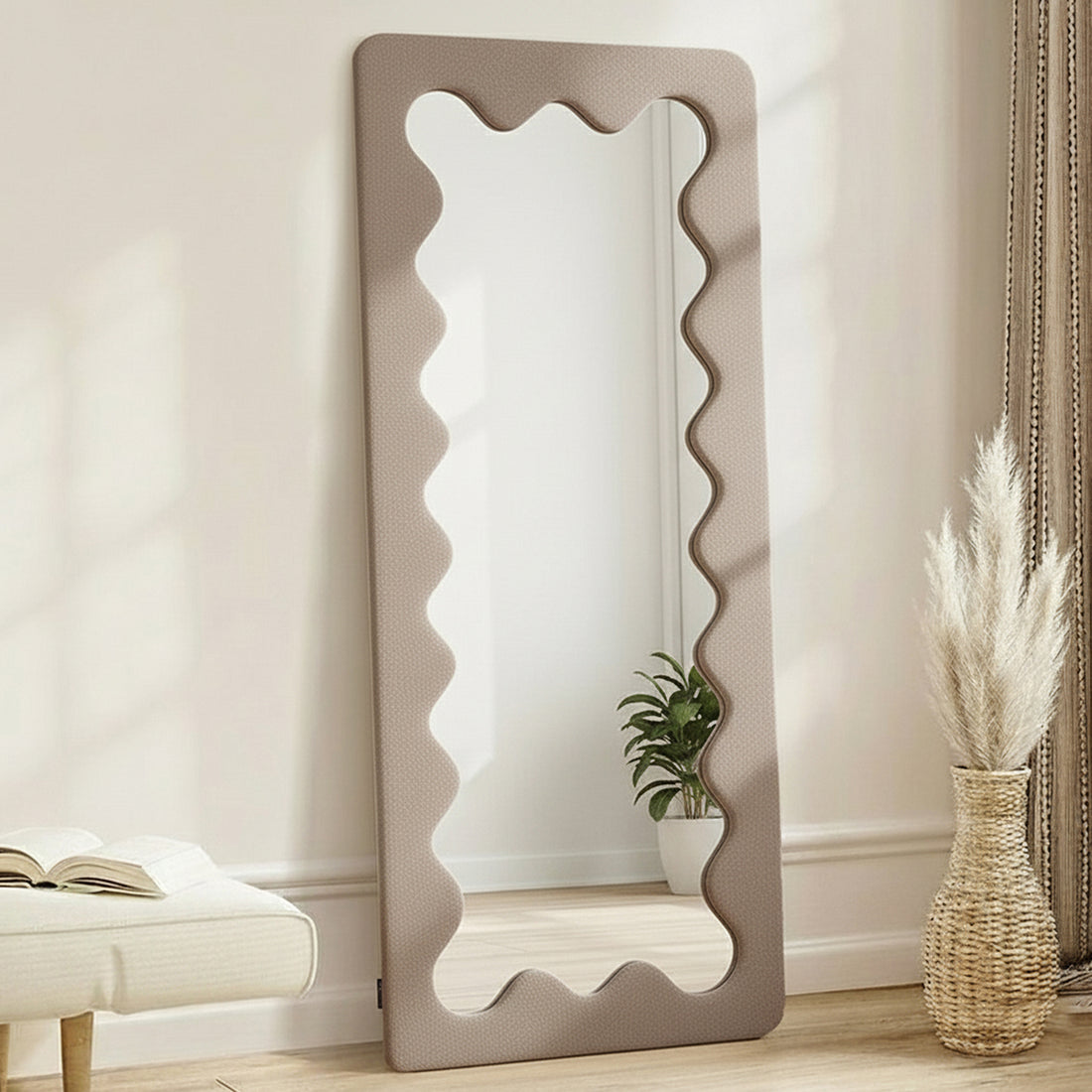 Serena 180cm Full Length Mirror in Taupe Brown with wavy-edged frame, styled with a bench, book, woven vase with dried grasses, and potted plant, creating a minimalist home decor vignette.