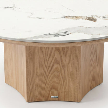 Close-up partial view of a round table with a marble-style top and light wood pedestal base on a white background.