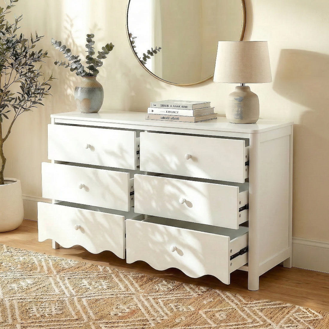 White dresser in inviting room setting with plant, books, lamp, and round mirror