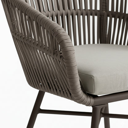 Marula Rope Outdoor Dining Chairs in Brown Set of 4 feature a dark tubular metal frame, woven rope back and armrests, and a light upholstered seat cushion, showcasing modern outdoor elegance.