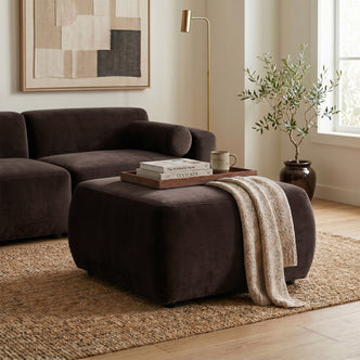 Dark brown upholstered ottoman in a styled living room setting