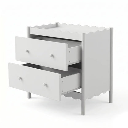 A white two-drawer baby change table featuring a decorative scalloped edge on the top surface and the base, complemented by simple round knobs.